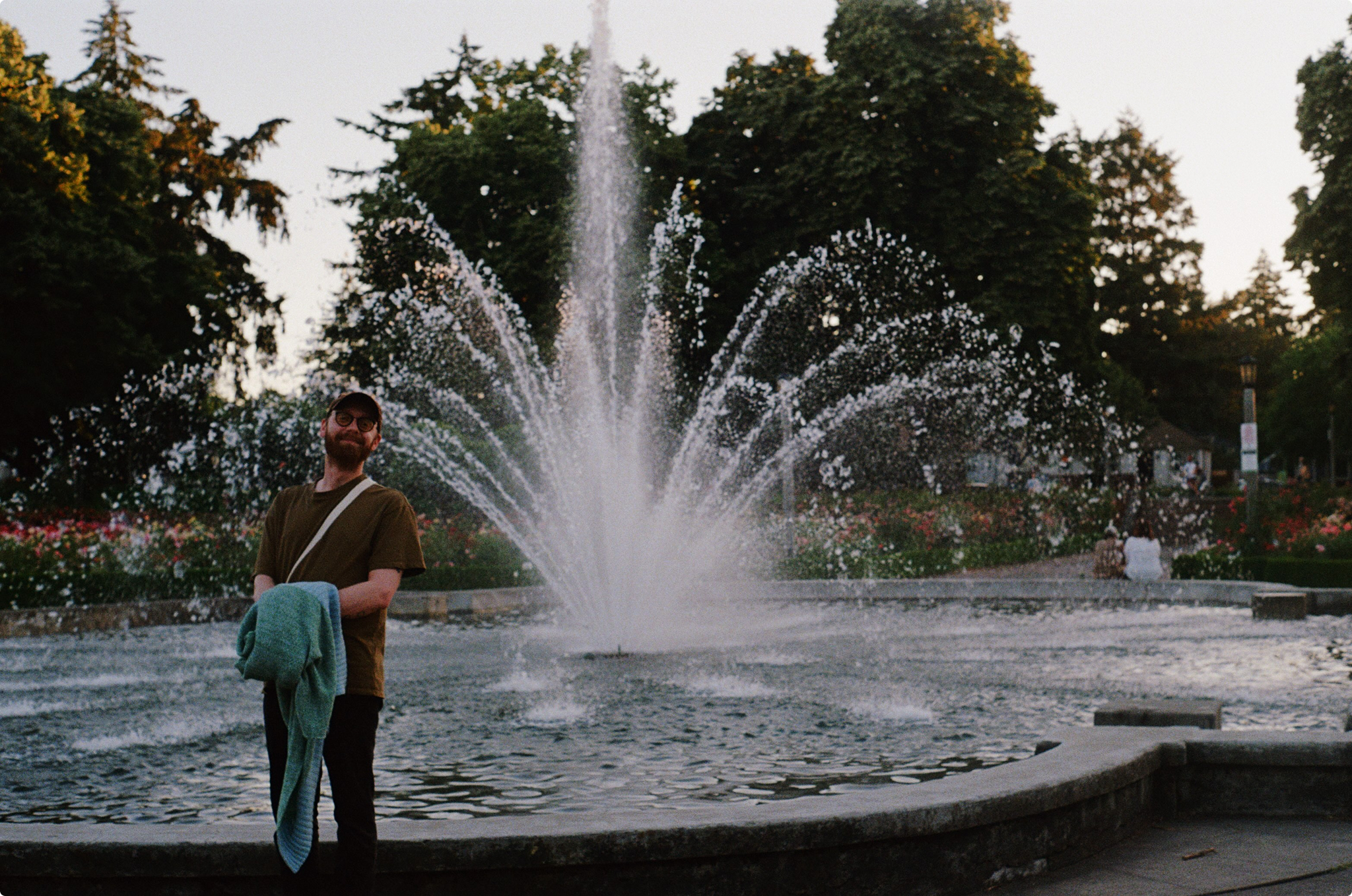 A man standing in front of a fountain in a park and smiling