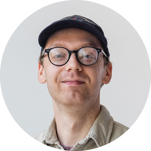 A professional headshot of a man wearing a baseball cap and smiling